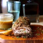 Pecan-Crusted Pork Tenderloin with Bourbon - Mustard Sauce on wood cutting board with pecans and fresh thyme scattered around it.