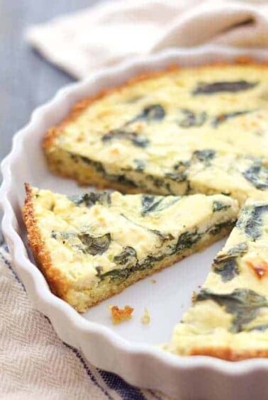 Spinach - Feta Quiche with Quinoa Crust in white baking dish with wedge removed.