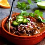 Feijoada (Brazilian Beef Stew) in red bowl garnished with jalapeno slices, cilantro and lime wedges.