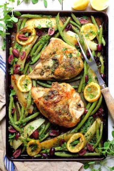 Sheet Pan Roast Chicken with Potatoes Green Beans Olives and Lemon on baking sheet with meat fork.