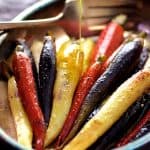 Roasted Carrots with Honey Curry Browned Butter in oval stainless steel baking dish being drizzled with butter.