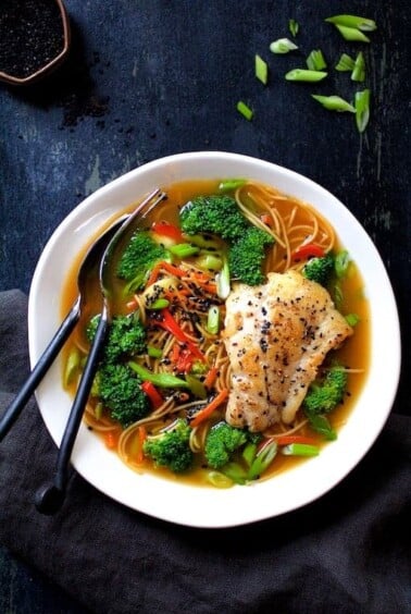 Asian Vegetable and Noodle Broth Bowls with Pan-Seared Fish in white bowl with fork and spoon.