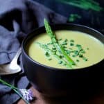 Cream of Asparagus Soup with Curry in black bowl garnished with fresh chives.