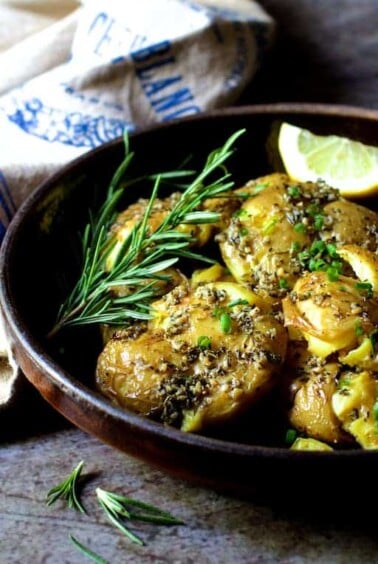 Rosemary Garlic Crushed Potatoes in brown ceramic dish garnished with fresh rosemary.