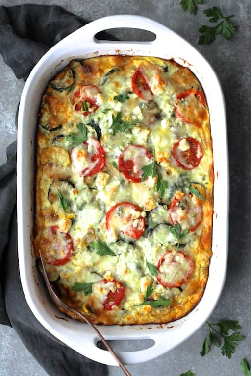 Four Cheese Strata with Zucchini and Tomatoes in white baking dish garnished with fresh parsley.