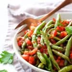 Green Beans with Tomato Caper Relish in white bowl on gray napkin with serving fork.