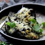 Two Quinoa Corn and Black Bean Stuffed Poblano Peppers in brown ceramic dish garnished with cilantro.