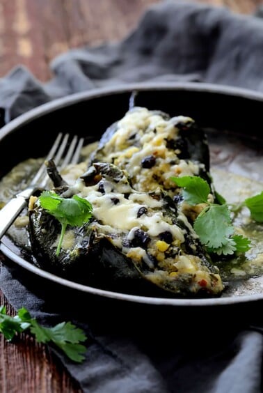 Two Quinoa Corn and Black Bean Stuffed Poblano Peppers in brown ceramic dish garnished with cilantro.