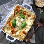 Lasagna with Pesto Green Beans and Potatoes in white baking dish on gray napkin.