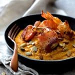 Pumpkin Chipotle and White Cheddar Grits with Bacon Wrapped Shrimp in black bowl garnished with pumpkin seeds.