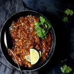 Slow Cooker Colorado Green Chili in black bowl garnished with lime wedges and cilantro sprigs.