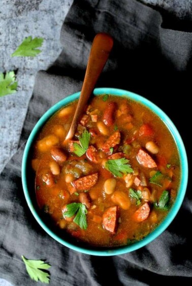 Slow Cooker Cajun 15 Bean Soup with Andouille Ham and Bacon in bright blue bowl with copper soup spoon.