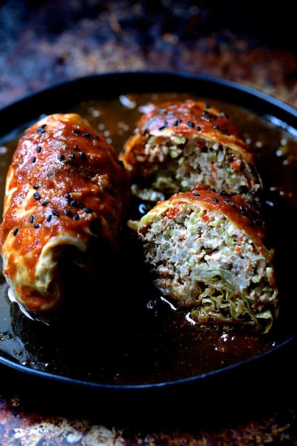 Photo showing Spicy Asian Pork Cabbage Rolls cut in half on black plate garnished with sesame seeds.
