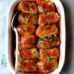 Spicy Asian Pork Cabbage Rolls in white baking dish with white serving spoon after being baked.