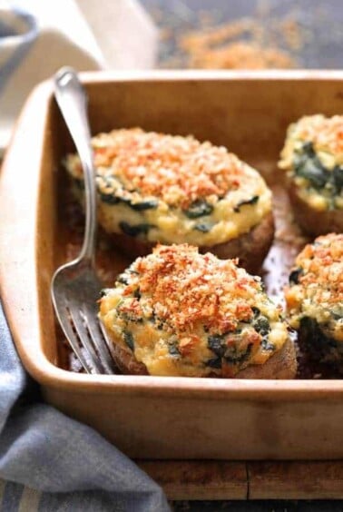 Spinach Parmesan Ranch Twice Baked Potatoes close up shot in clay baking dish with serving fork and blue striped towel.