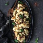 Roasted Cauliflower with Black Olive Pangrattato \on black platter with copper serving fork and black striped towel.