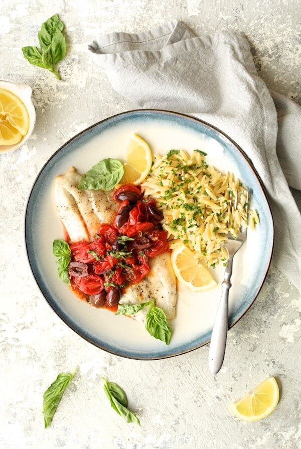 Baked Fish with Cherry Tomato and Olive Sauce and Lemon Chive Asiago Orzo hero shot on blue-rimmed plate