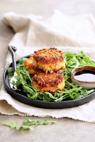 Tuna Kimchi Cakes with Soy Ginger Dipping Sauce on black plate over arugula.