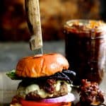 Grilled Burgers with Bacon Tomato Jam and Smoked Gouda with a steak knife through the burger and the jar of jam.