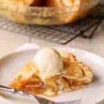 Slice of apple pie on white plate with vanilla ice cream.