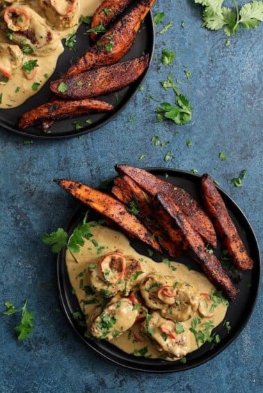 Two servings of Spicy Tahini Pork Medallions with Harissa Roasted Sweet Potato Wedges on black plates.