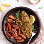 One serving of Pistachio-Crusted Fish with Lemon-Dill Aioli with roasted potatoes on black dinner plate.