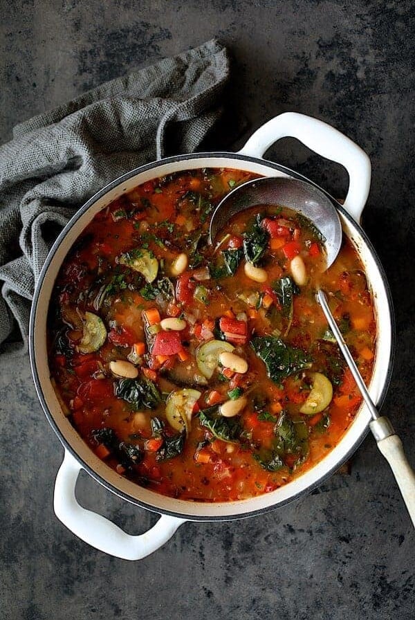 Smoky Spanish Vegetable and White Bean Soup with Kale in white Dutch oven.