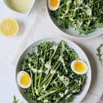 Two servings of Arugula, Egg and Asparagus Salad with Creamy Lemon Vinaigrette in white bowls.
