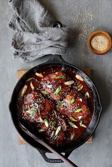 Korean Braised Chicken Thighs in cast iron skillet garnished with scallion and sesame seeds.