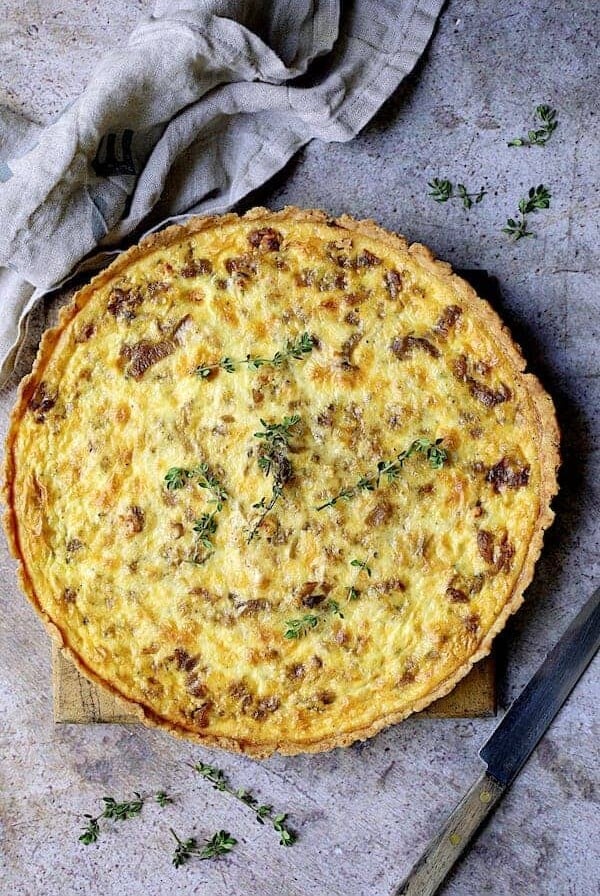 Whole baked Caramelized Onion and Goat Cheese Tart on wood cutting board.