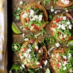 Six Chicken Tostadas with Black Bean Guacamole and Salsa Fresca on wood serving tray.