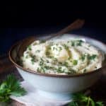 Celery root puree in bowl garnished with fresh chopped parsley.