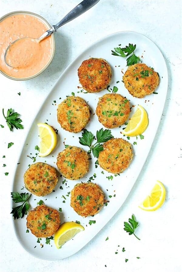 Nine shrimp cakes on oval white platter garnished with lemon and parsley.