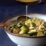 Browned butter being drizzled over roasted Brussels sprouts in pale green bowl.