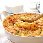 Spicy Shrimp and Grits Casserole with Gouda Cheese in a round white baking dish with a wooden spoon scooping some out.