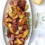 Duck Fat Roasted Fingerlings with Sausage on oval white platter garnished with fresh rosemary.