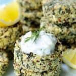 Two Greek Quinoa Cakes with Tzatziki stacked with tzatziki, garnished with lemon wedges and dill sprigs.
