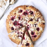 Raspberry Ricotta Cake with Almonds - Overhead hero shot of cake on white paper with two pieces cut into it and almonds scattered about
