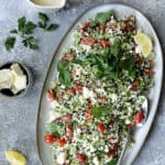 Cauliflower Tabouli with Lemon Tahini Dressing and Feta Cheese - Overhead hero shot of salad on large oval platter garnished with parsley and lemons