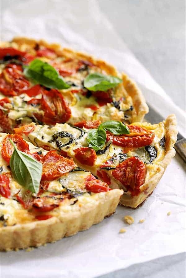 Provencal Vegetable and Goat Cheese Tart - Hero shot of tart on white parchment paper with a slice removed