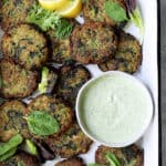 Zucchini Red Lentil Fritters with Cilantro Yogurt Sauce - Overhead shot in white pan with sauce garnished with greens and lemons