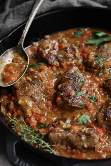 Cajun-Smothered Pork Medallions - Close-up shot in cast iron skillet with thyme sprigs