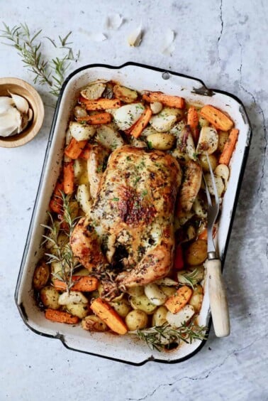 Photo of Garlic Herb Butter Roast Chicken with Root Vegetables in white distressed roasting pan.