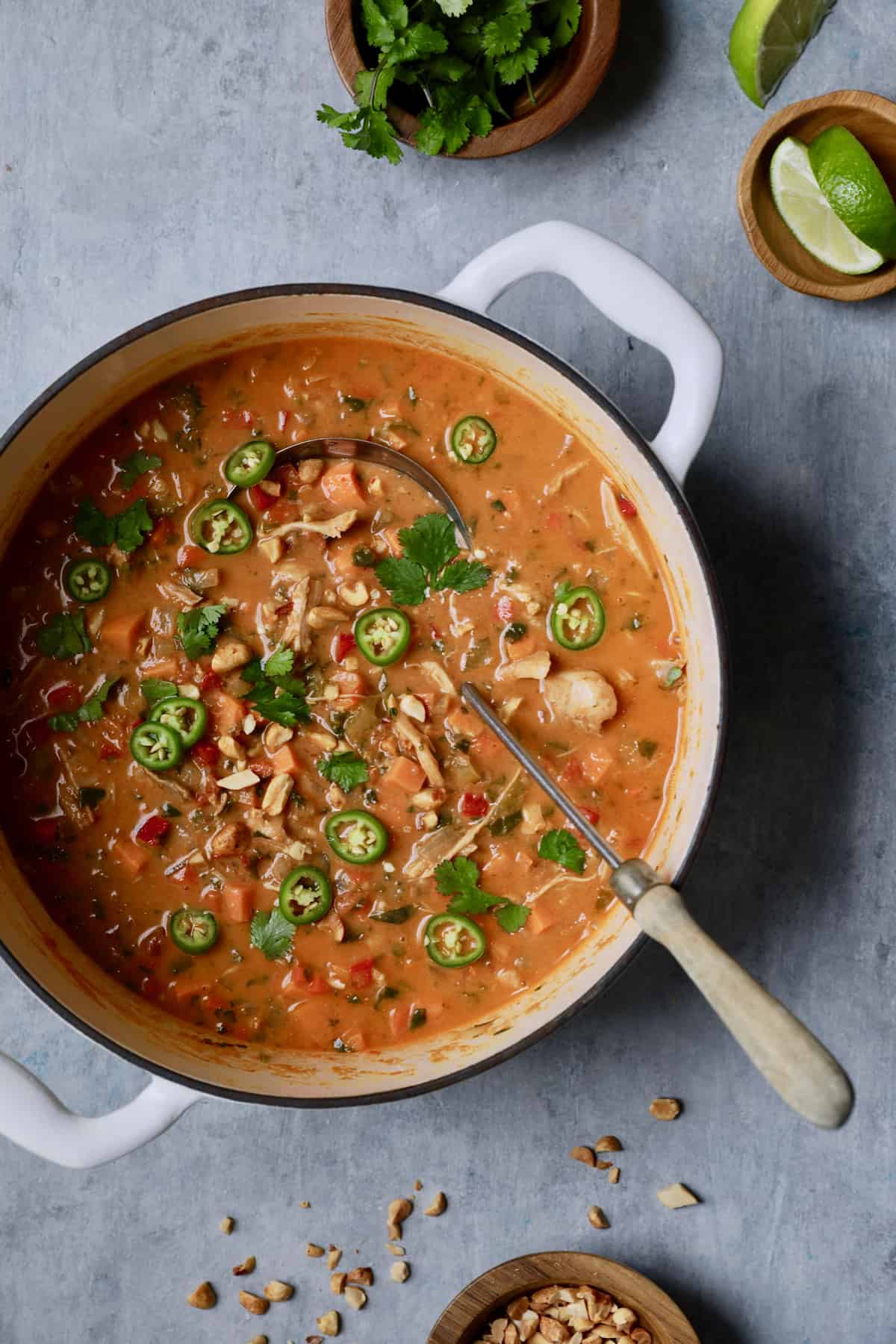 Photo of Spicy Chicken, Sweet Potato and Peanut Soup in white Dutch oven garnished with cilantro and green chiles.