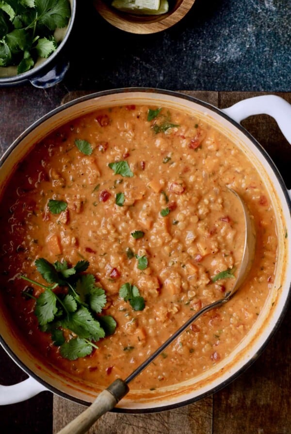 Photo of Thai Red Curry Sweet Potato and Lentil Soup in white Dutch oven with soup ladle.