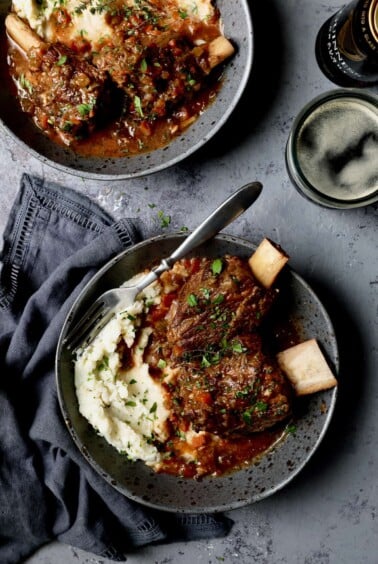 Photo of Stout Braised Beef Short Ribs and Colcannon on gray background with blue napkin and glass of beer.