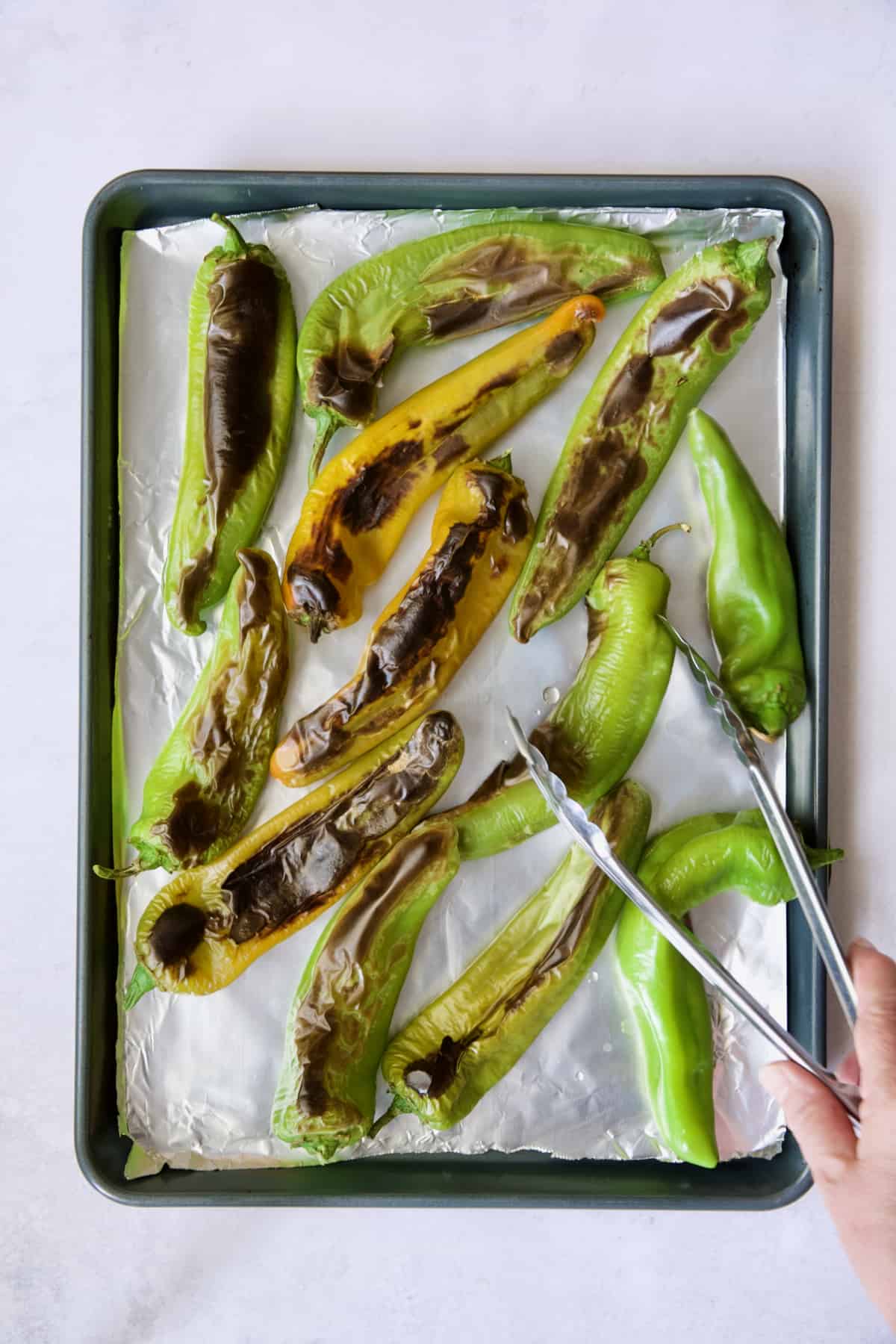 Half roasted Hatch green chiles being turned with tongs.