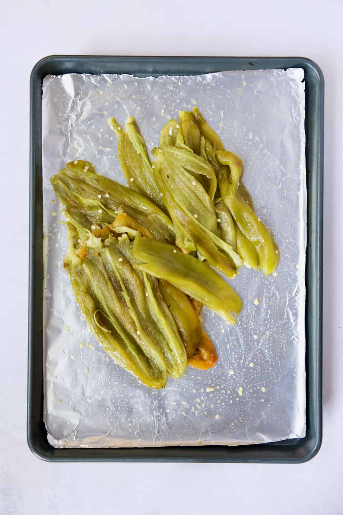 Pile of roasted and seeded Hatch green chiles on rimmed sheet pan.