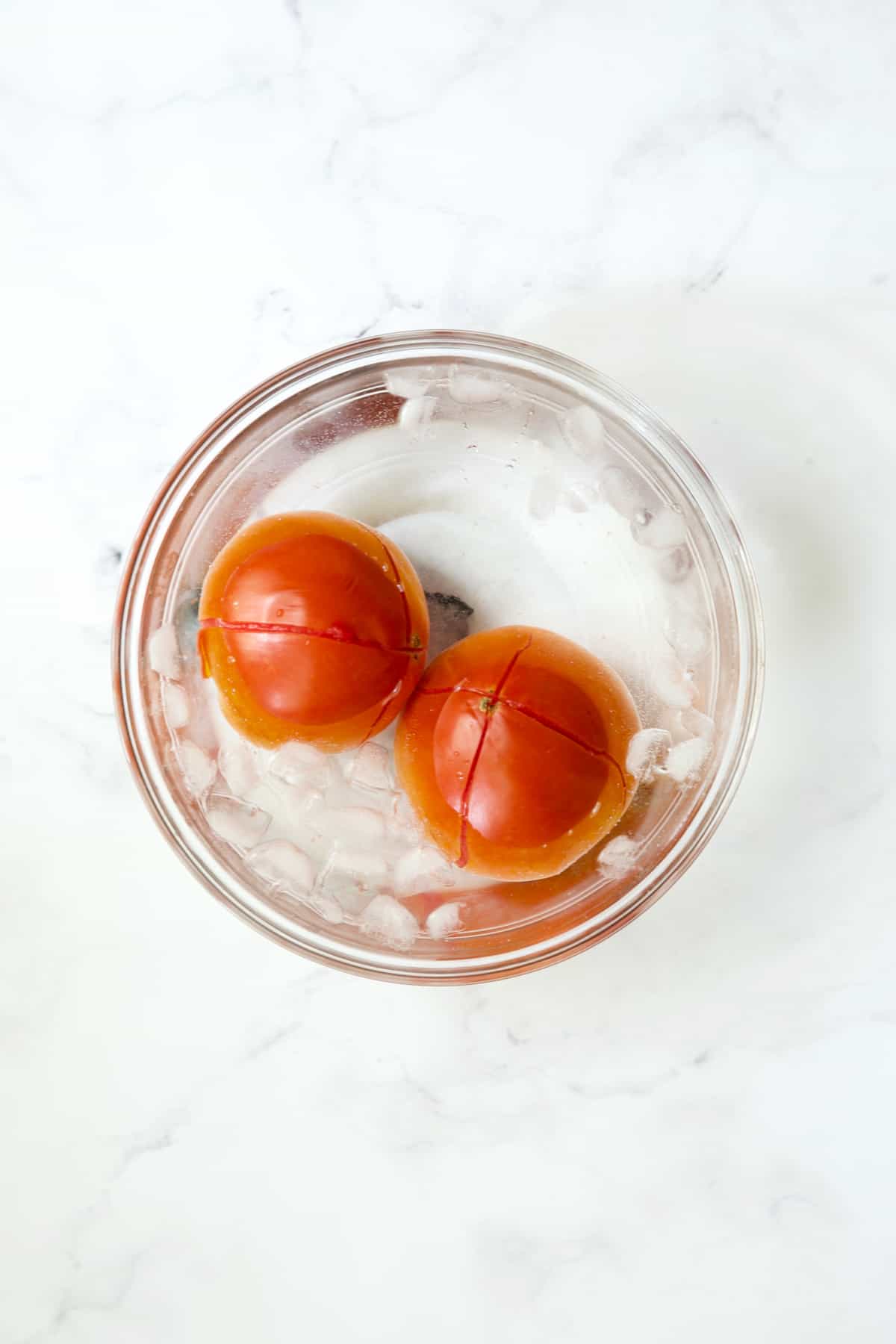 Two tomatoes in ice bath in glass bowl.