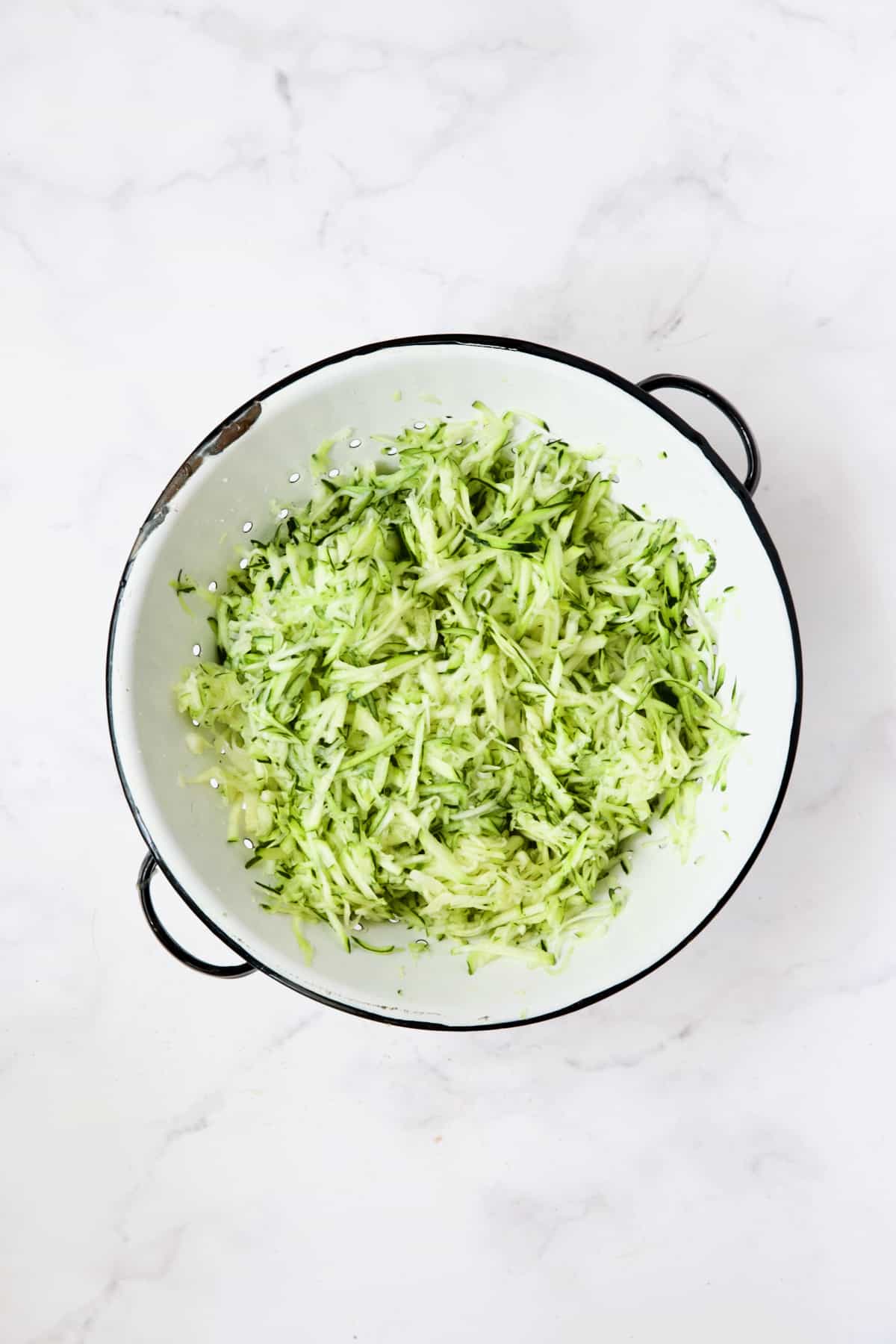Shredded zucchini in vintage white colander.